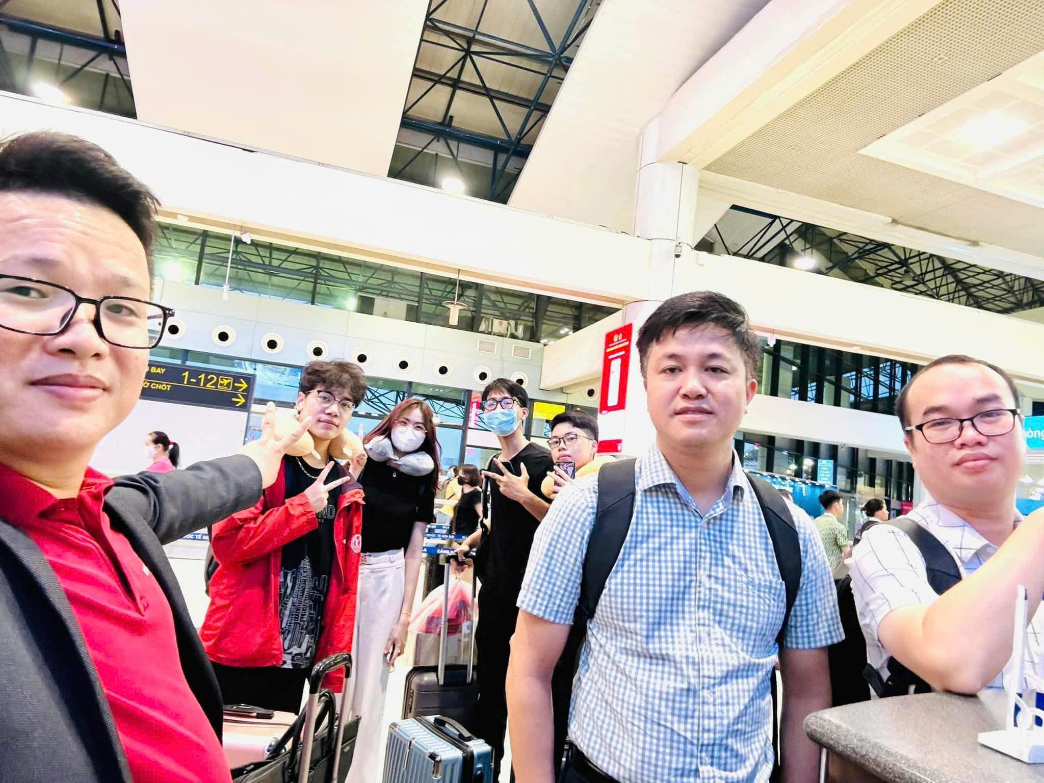 Ảnh selfie cả nhóm ở sảnh sân bay Nội Bài, vali kéo bên cạnh, vài người đeo gối cổ chờ giờ bay.